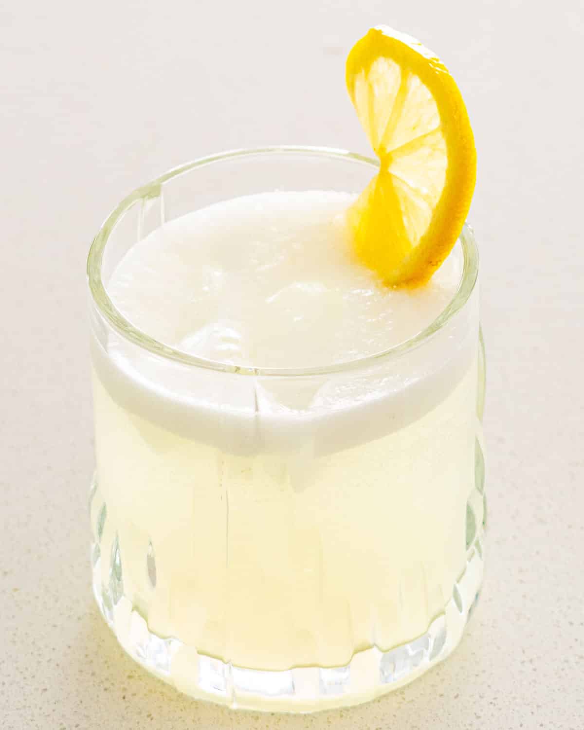 a glass filled with gin fizz and garnished with a lemon slice.