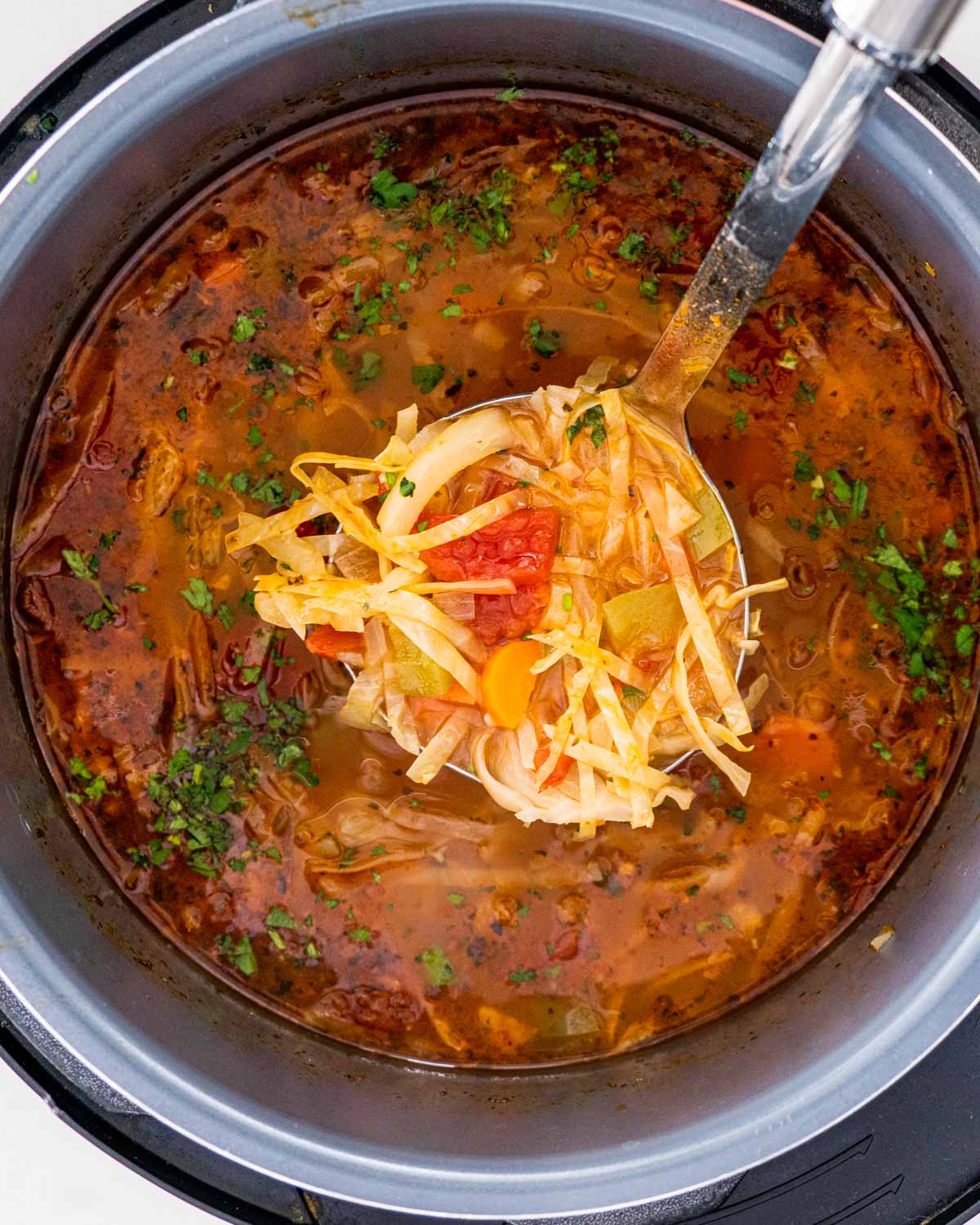 cabbage soup in an instant pot with a ladle lifting some up.