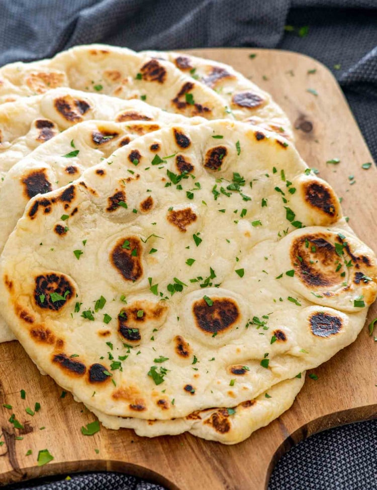 a stack of naan bread on a cutting board garnished with parsley.