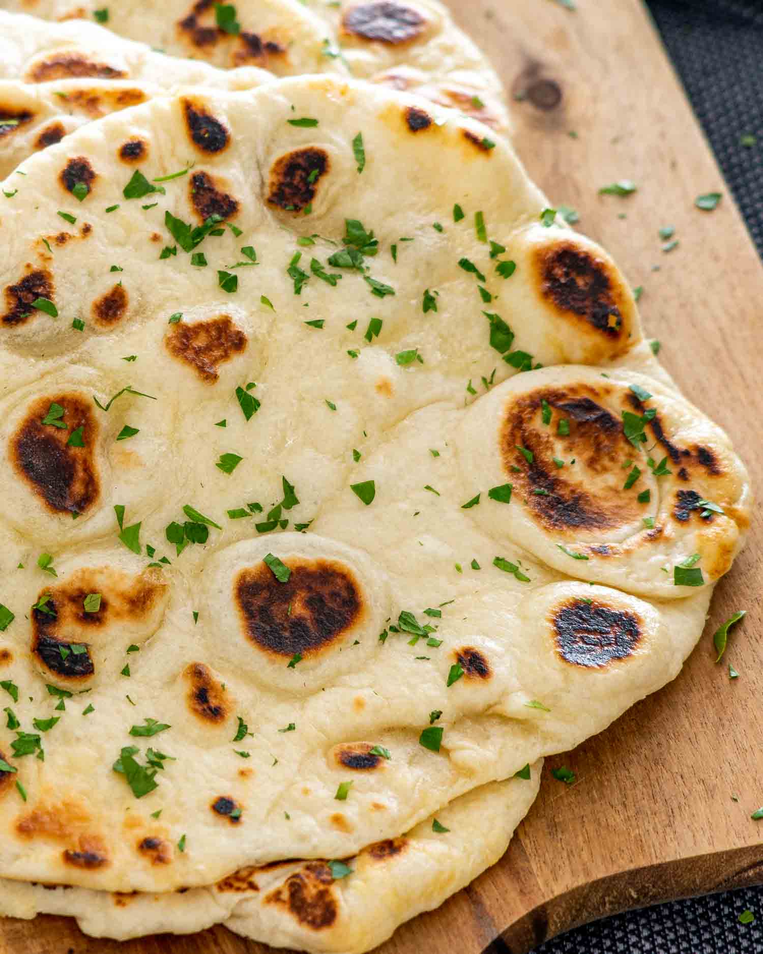 a stack of naan bread on a cutting board garnished with parsley.