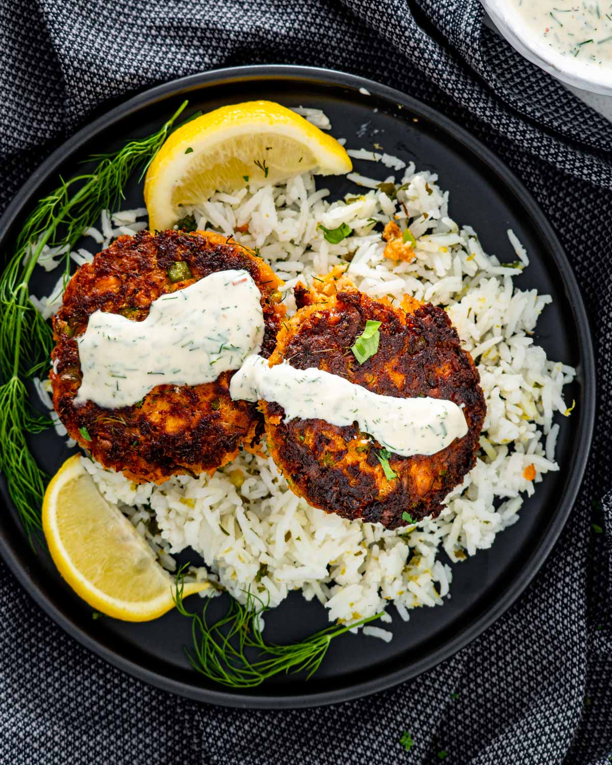 two salmon patties with dill sauce over a bed of rice.