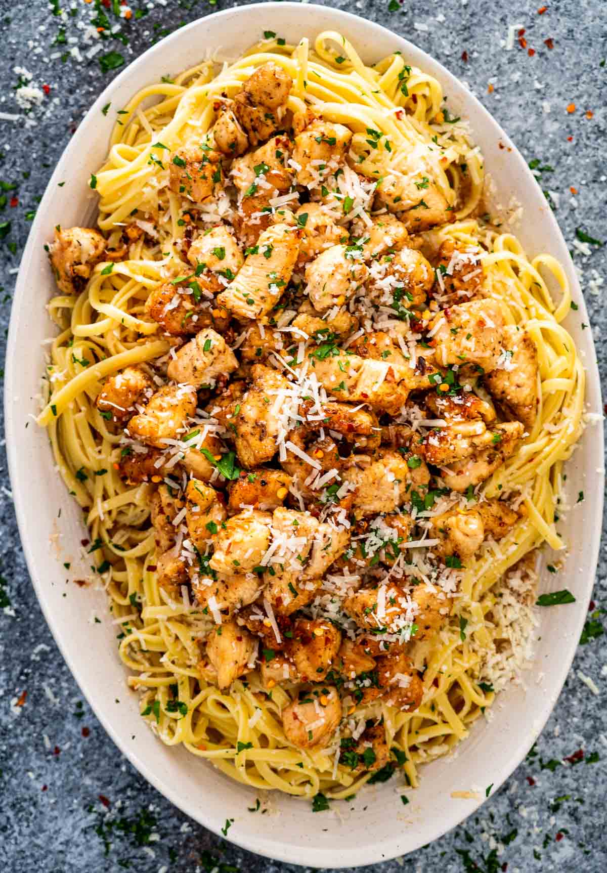 chicken scampi with linguini garnished with parmesan cheese on a white platter.