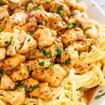 chicken scampi with linguini garnished with parmesan cheese on a white platter.
