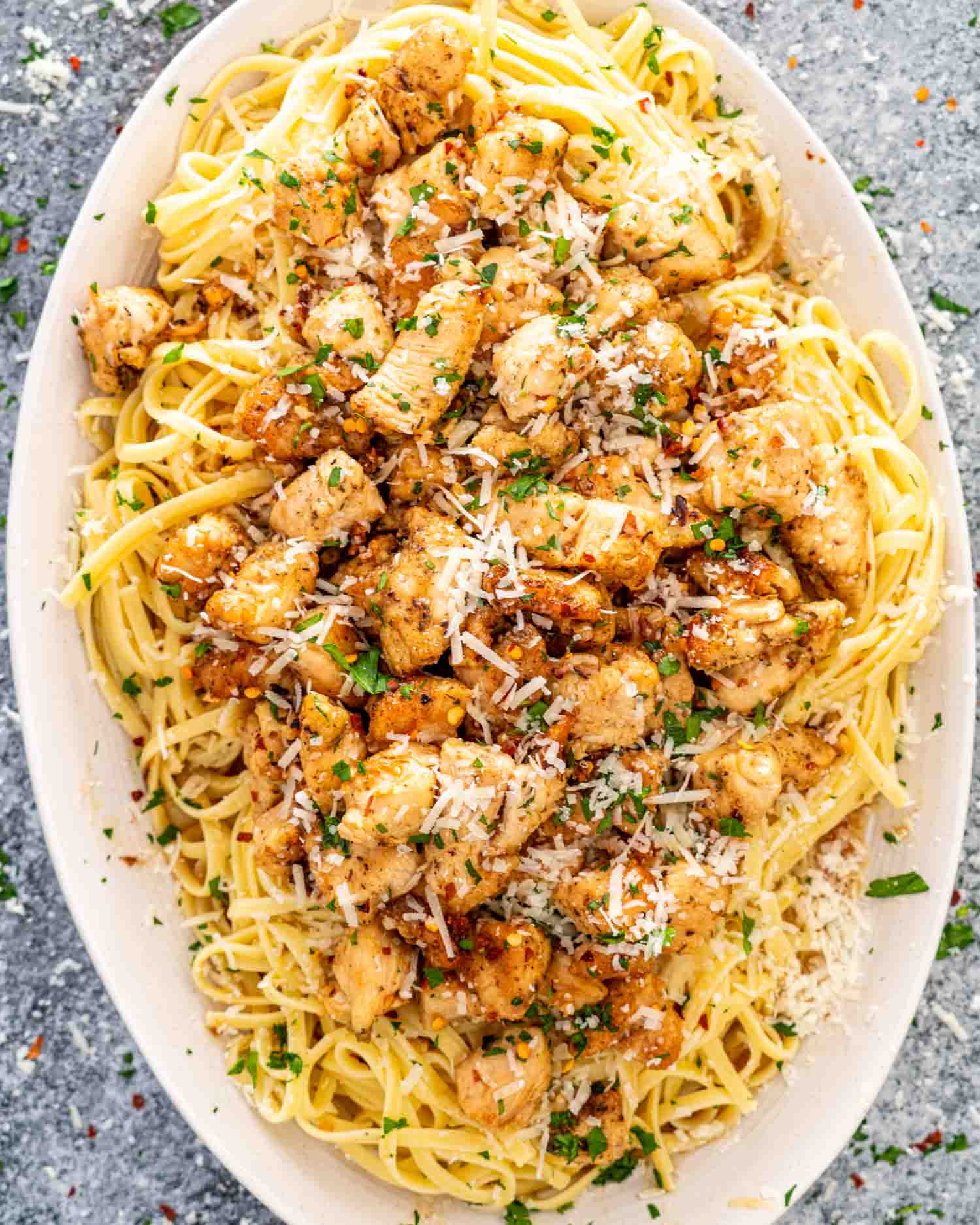 chicken scampi with linguini garnished with parmesan cheese on a white platter.