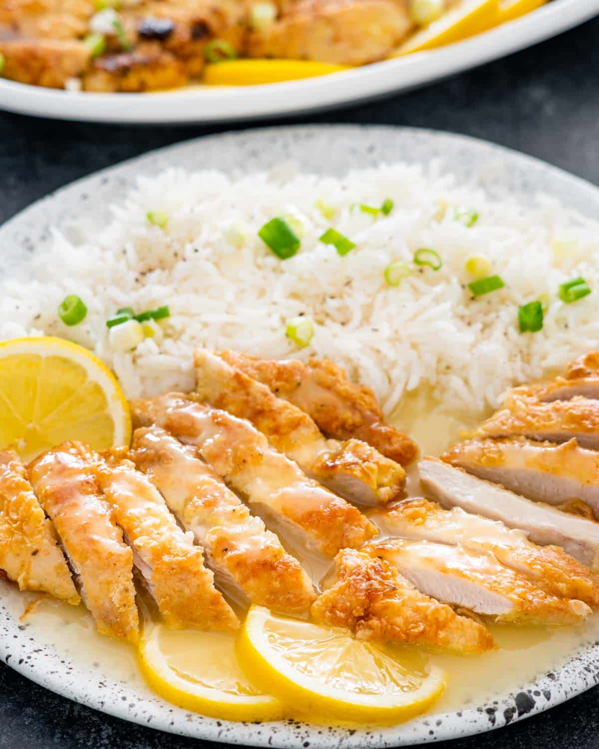 sliced up chinese lemon chicken with a side of rice and garnished with lemon slices.