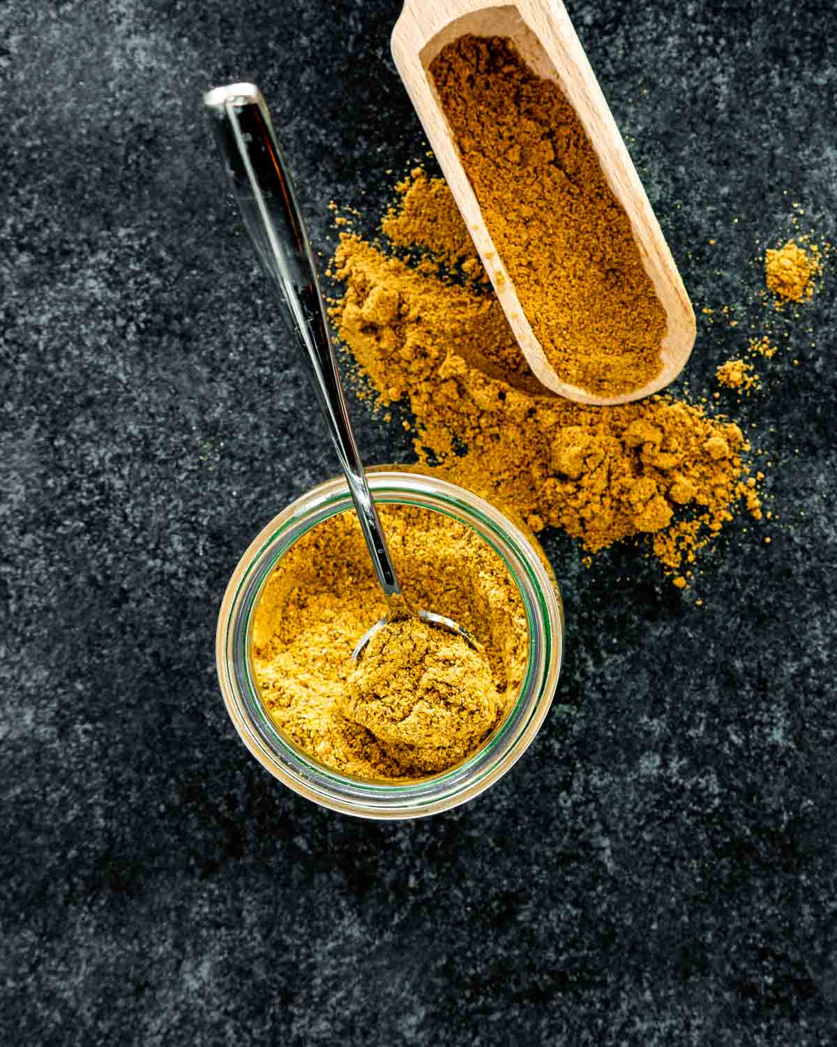 overhead shot of curry powder in a jar with a spoon inside.