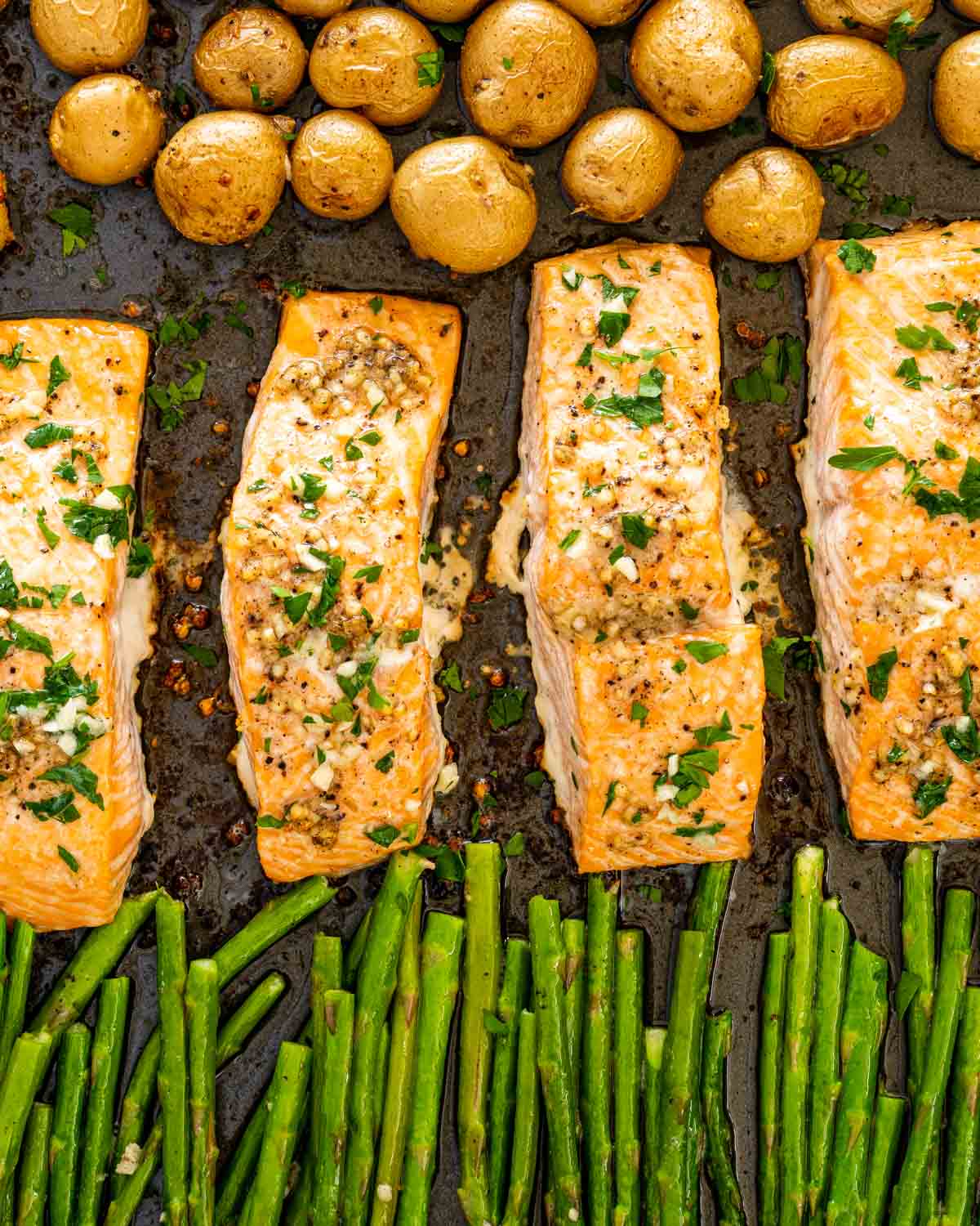 garlic butter salmon with asparagus and baby potatoes on a sheet pan.