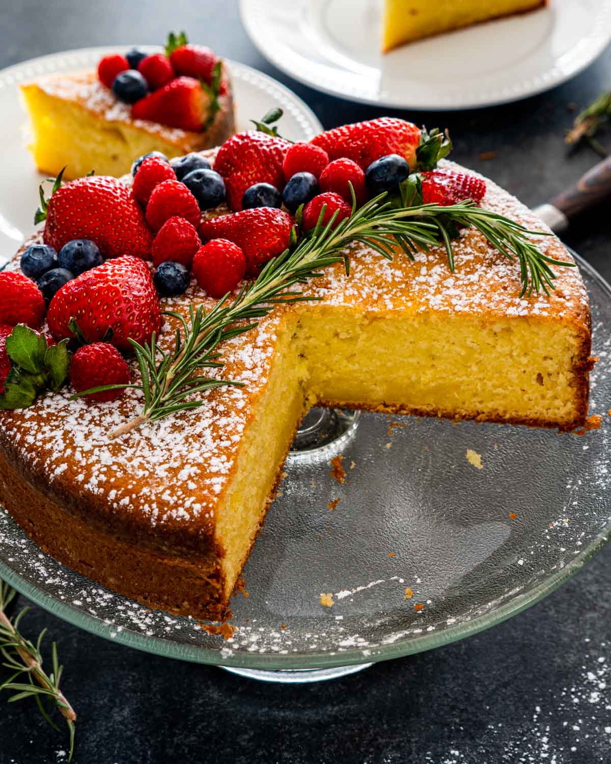 olive oil cake with a few slices cut out of it on a cake platter garnished with berries.