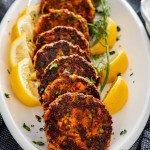 a stack of salmon patties on a serving platter garnished with lemon wedges and dill.