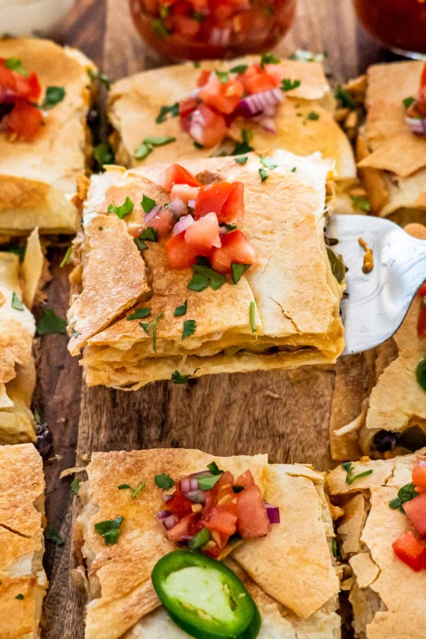 sheet pan quesadilla cut into pieces on a cutting board topped with pico de gallo.