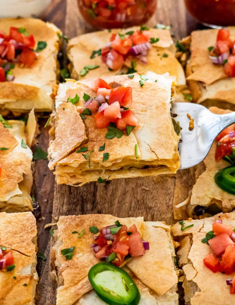 sheet pan quesadilla cut into pieces on a cutting board topped with pico de gallo.