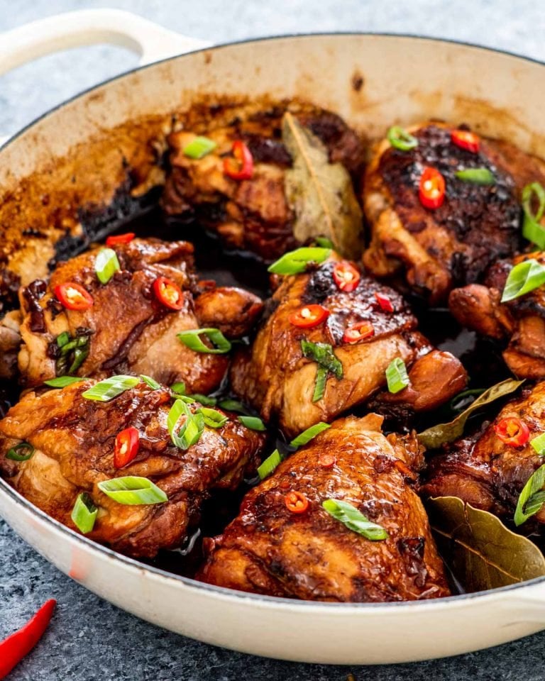 chicken adobo in a braiser garnished with green onions and red chilies.