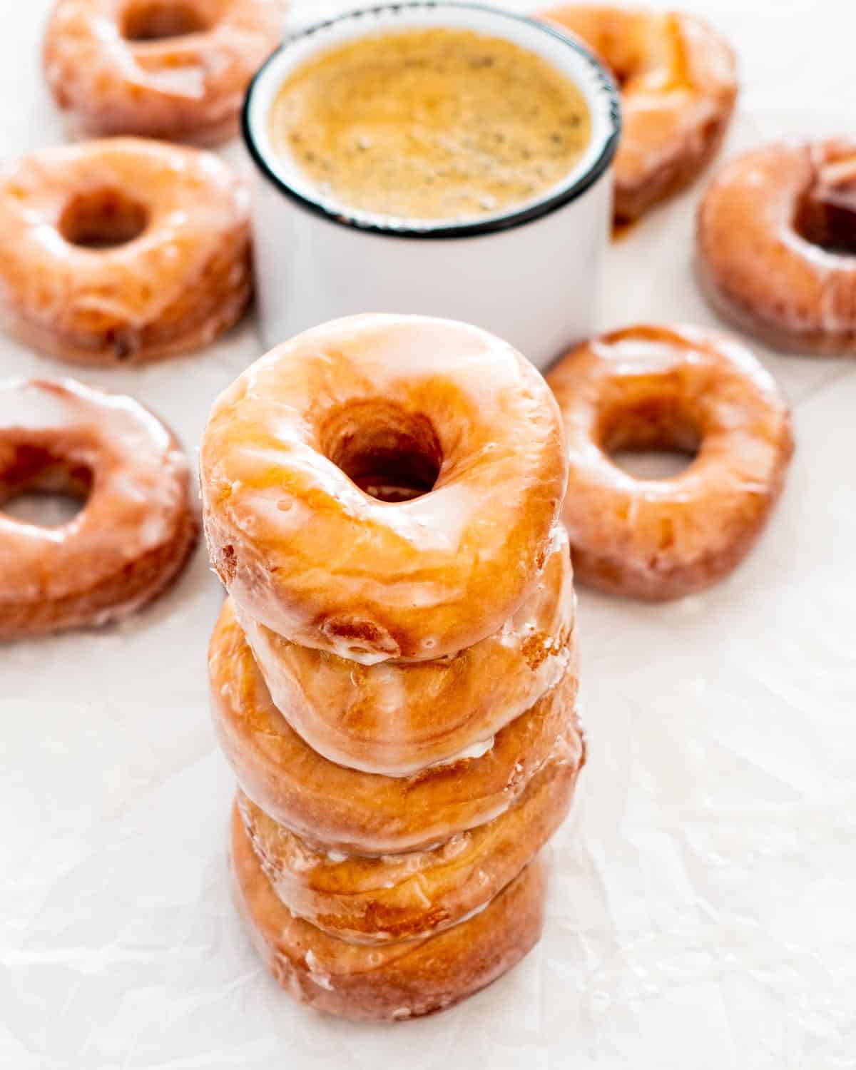 a stack of glazed donuts with a cup of coffee in the background.