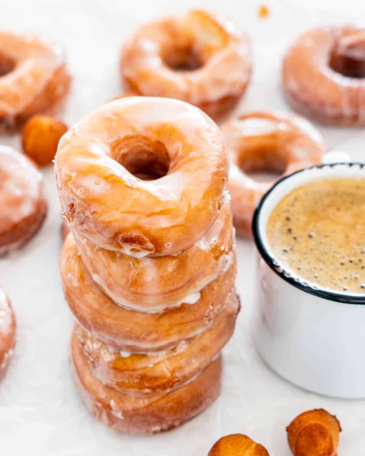 a stack of glazed donuts next to a cup of coffee.