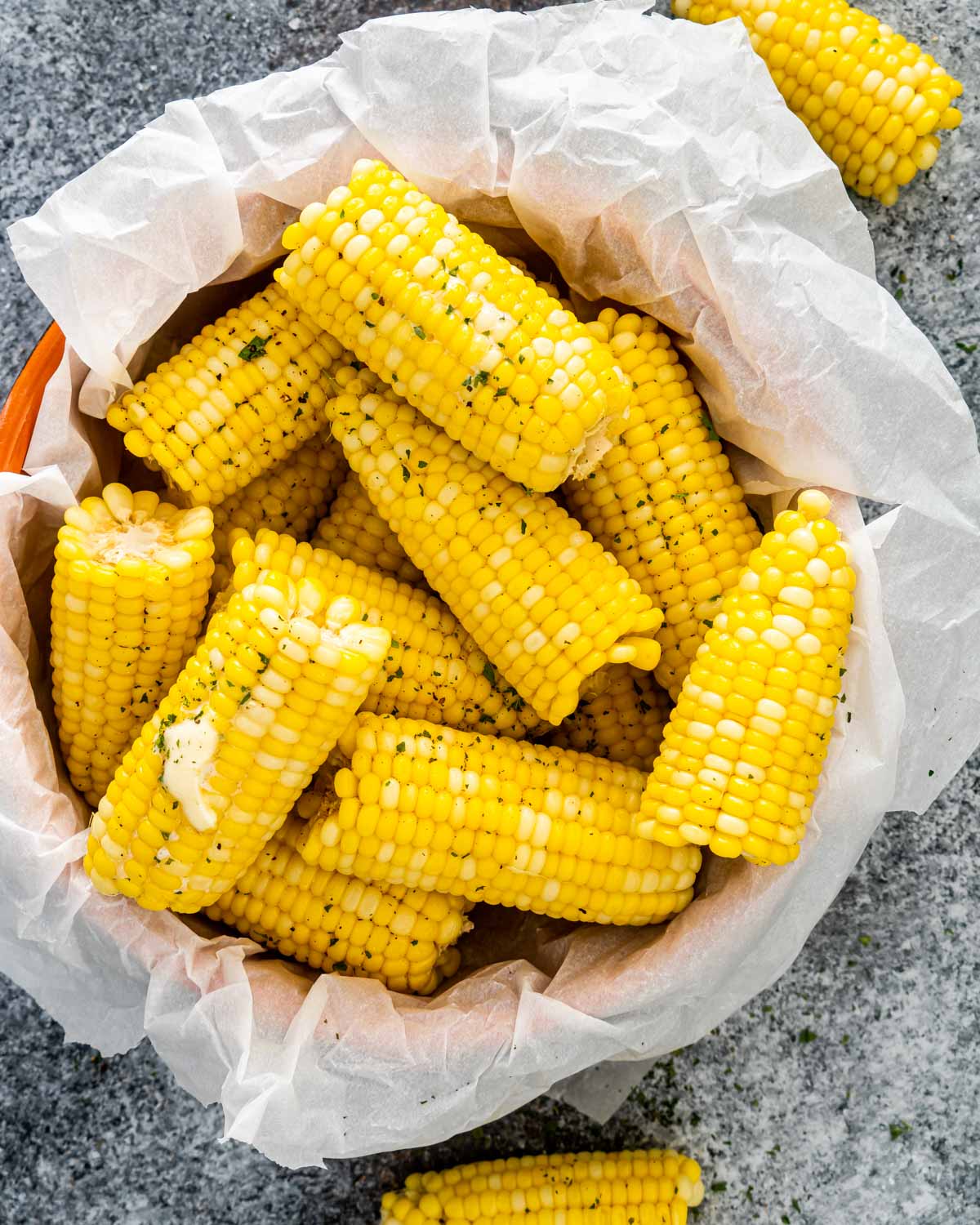 corn on the cob in a basket with parchment paper some with a pat of butter.