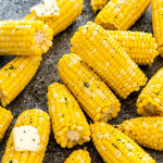 a few corn on a table some with a pat of butter.