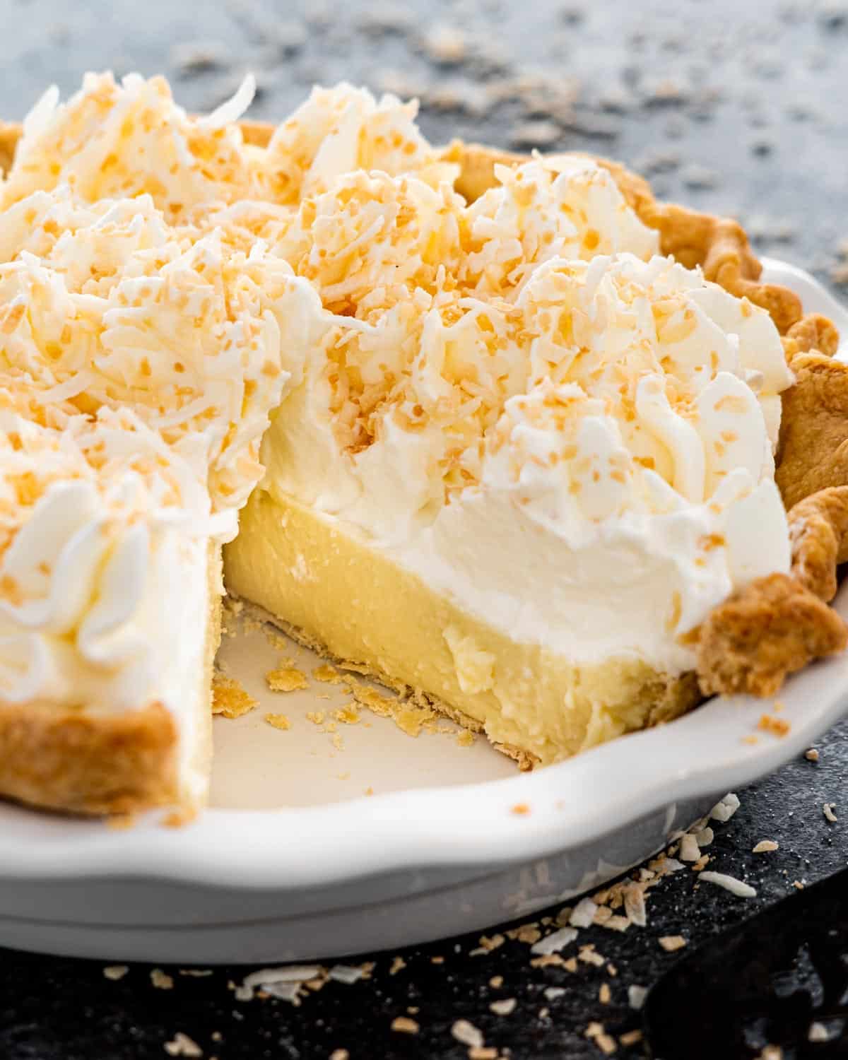 a coconut cream pie in a pie plate with a piece missing.