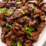 korean beef bulgogi garnished with green onions on a white serving platter.