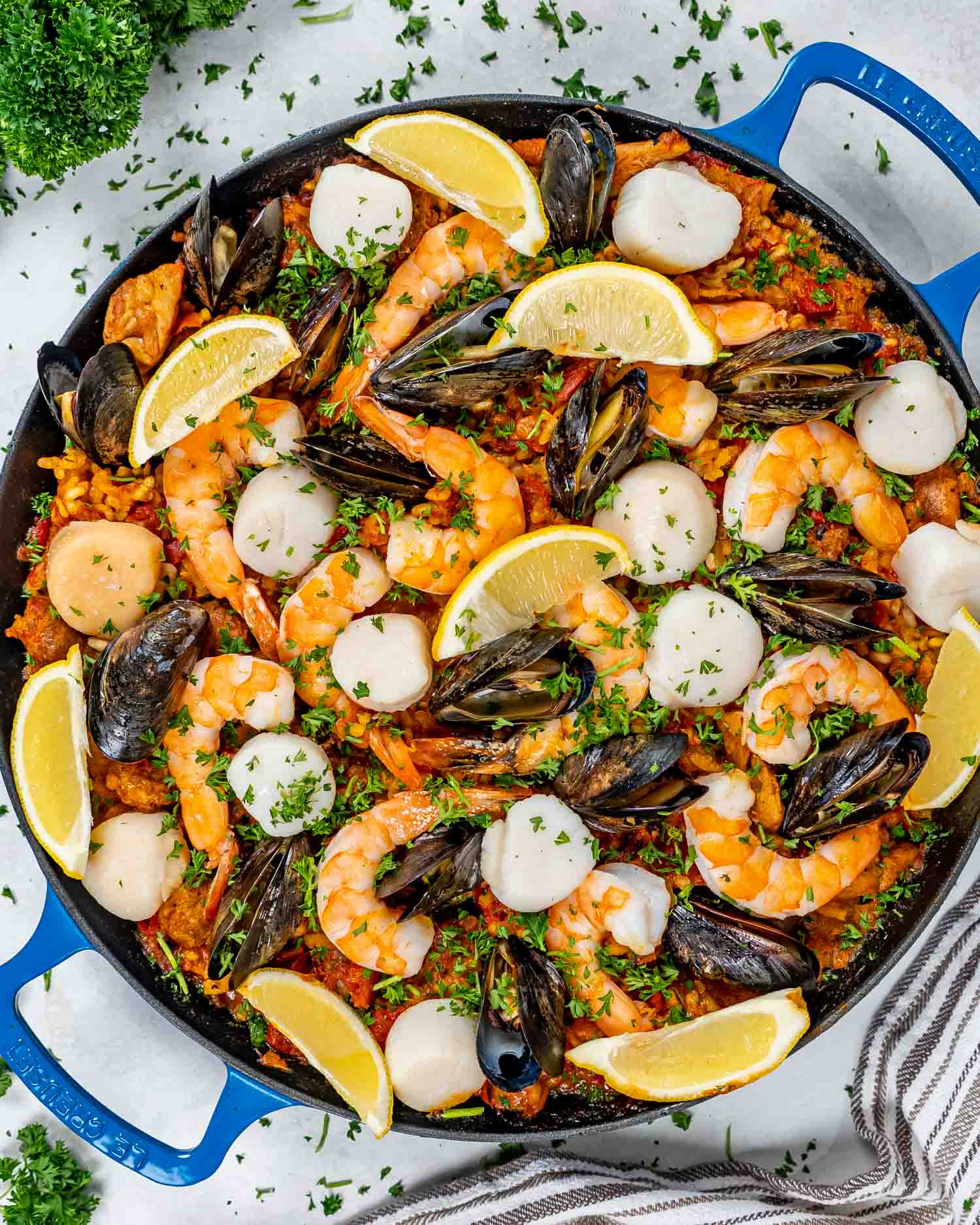 freshly made paella in a paella pan garnished with lemons and parsley.