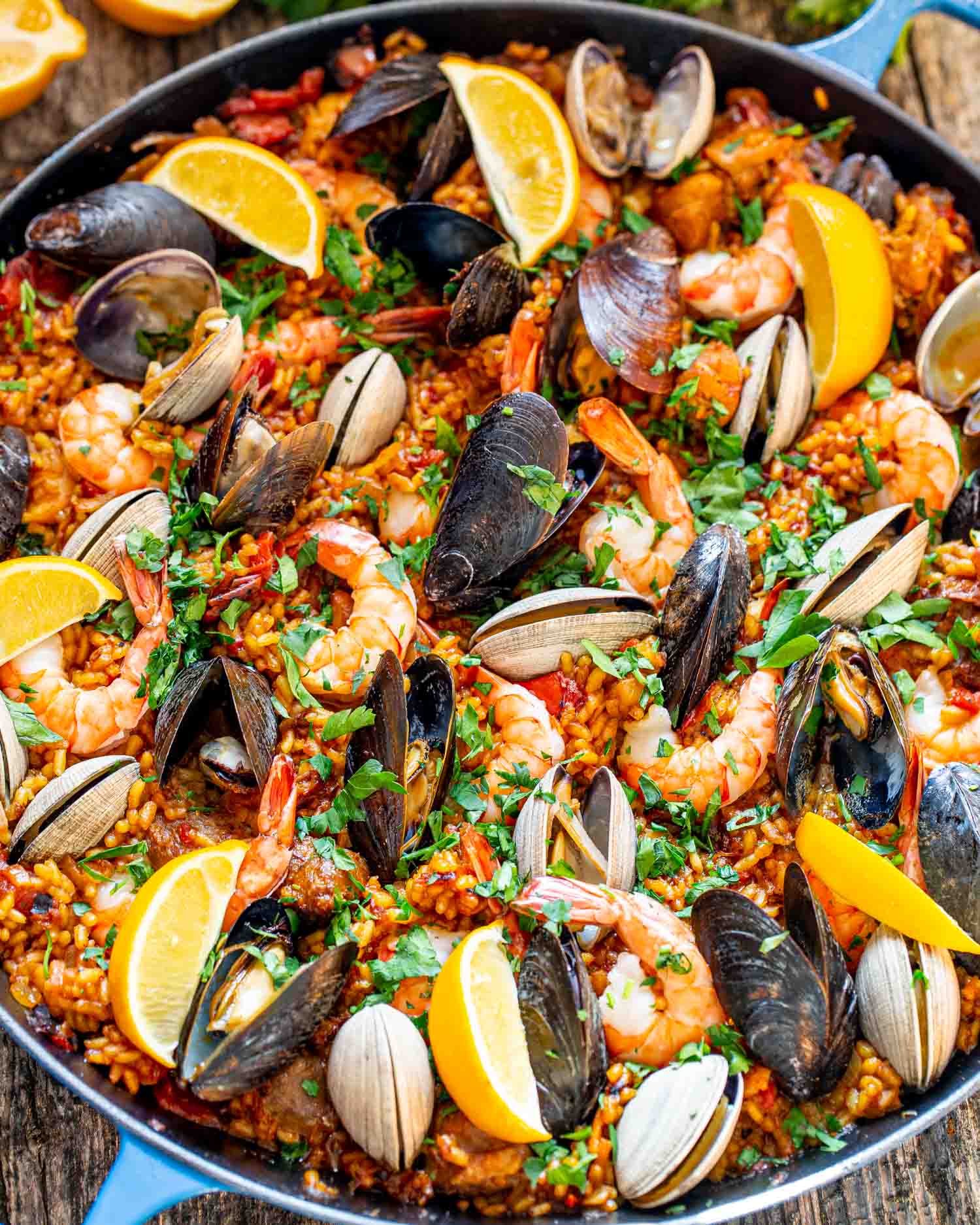 freshly made paella in a paella pan garnished with lemons and parsley.