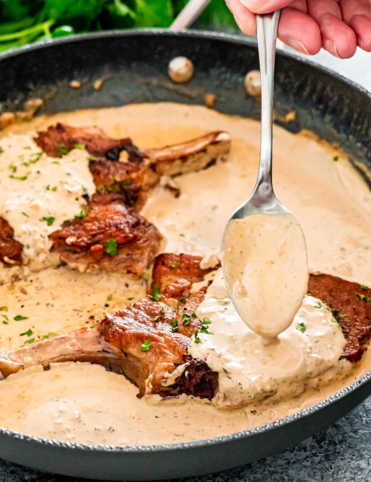 spooning peppercorn sauce over pork chops in a skillet.