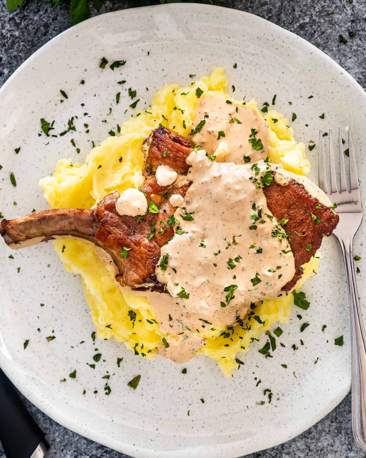 a pork chop over a bed of mashed potatoes with peppercorn sauce.