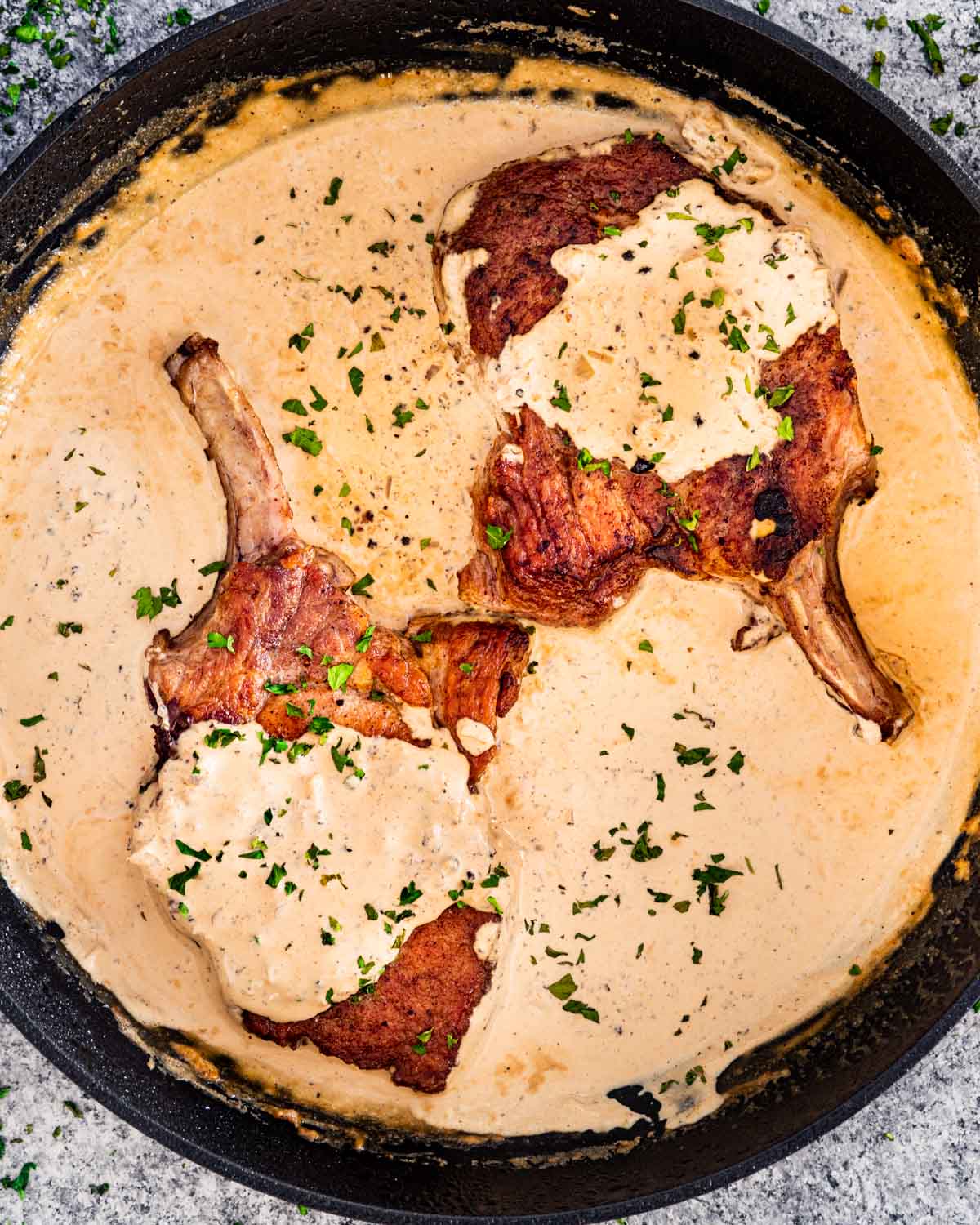 pork chops with peppercorn sauce in a black skillet garnished with parsley.