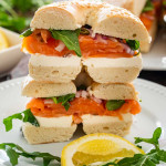 salmon cream cheese bagel on a white plate garnished with lemon wedge.