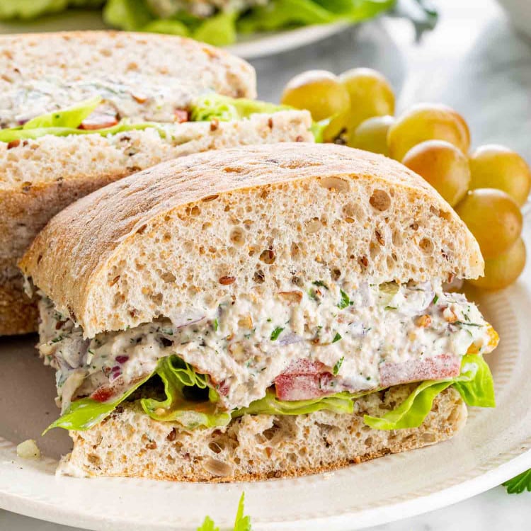 side view shot of a tuna salad sandwich on a plate with grapes.