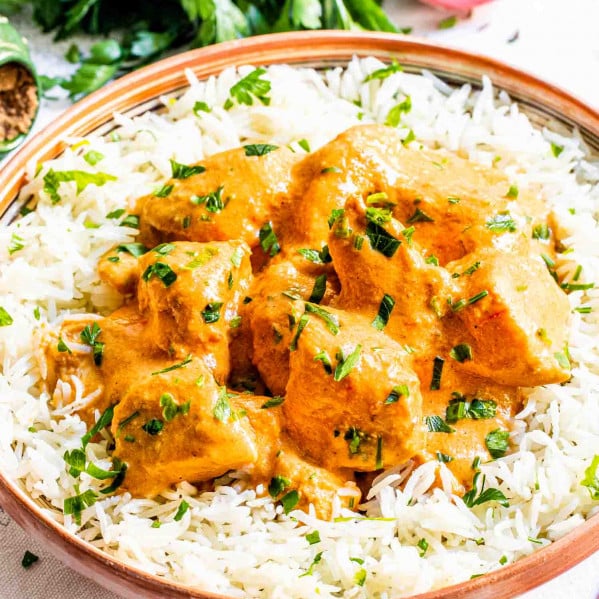 butter chicken over a bed of rice in a plate garnished with cilantro.