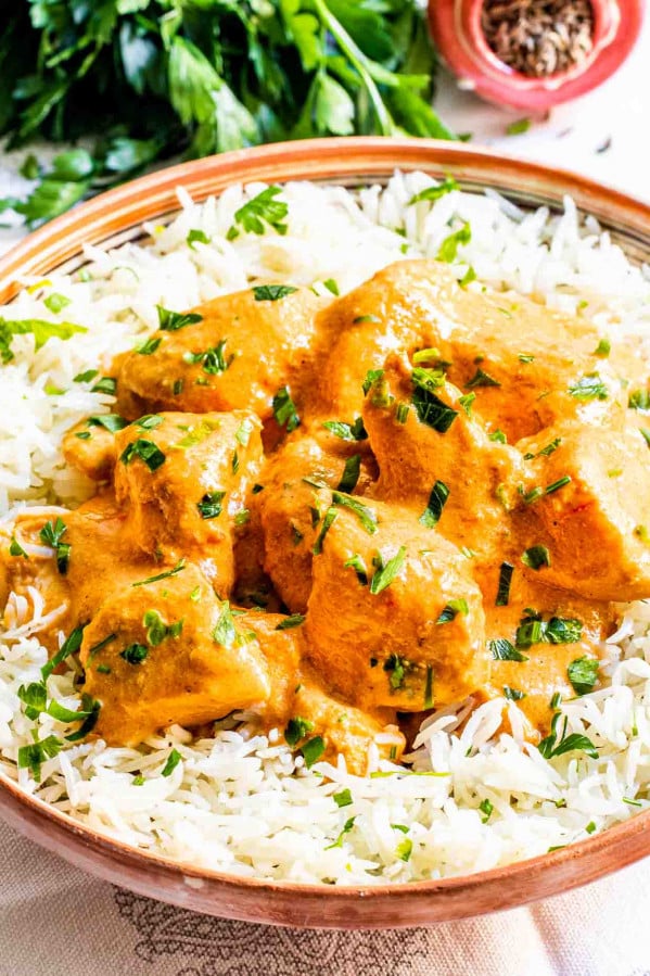 butter chicken over a bed of rice in a plate garnished with cilantro.