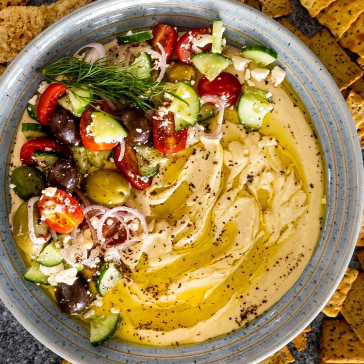 freshly made hummus drizzled with olive oil and garnished with tomatoes cucumbers and olives.