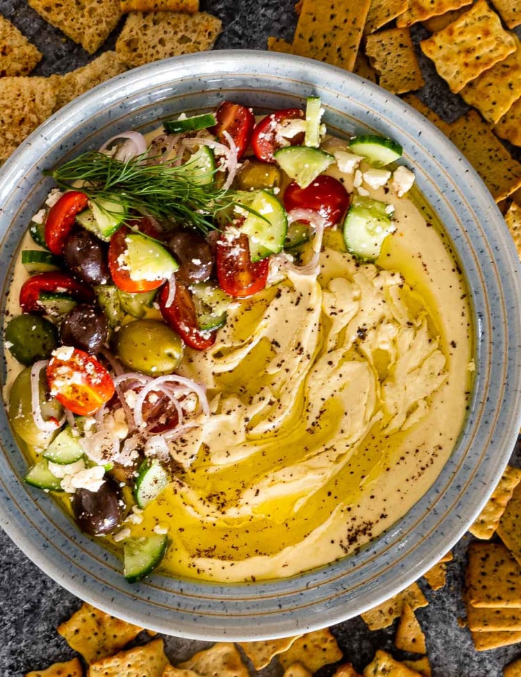 freshly made hummus drizzled with olive oil and garnished with tomatoes cucumbers and olives.