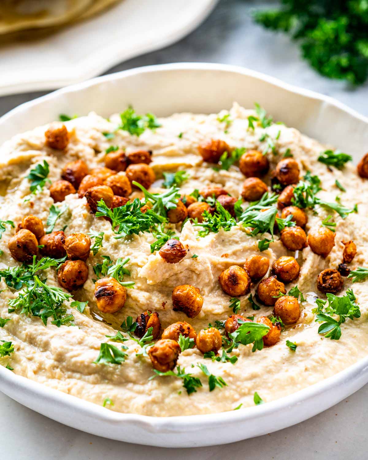hummus in a plate garnished with parsley and toasted garbanzo beans.