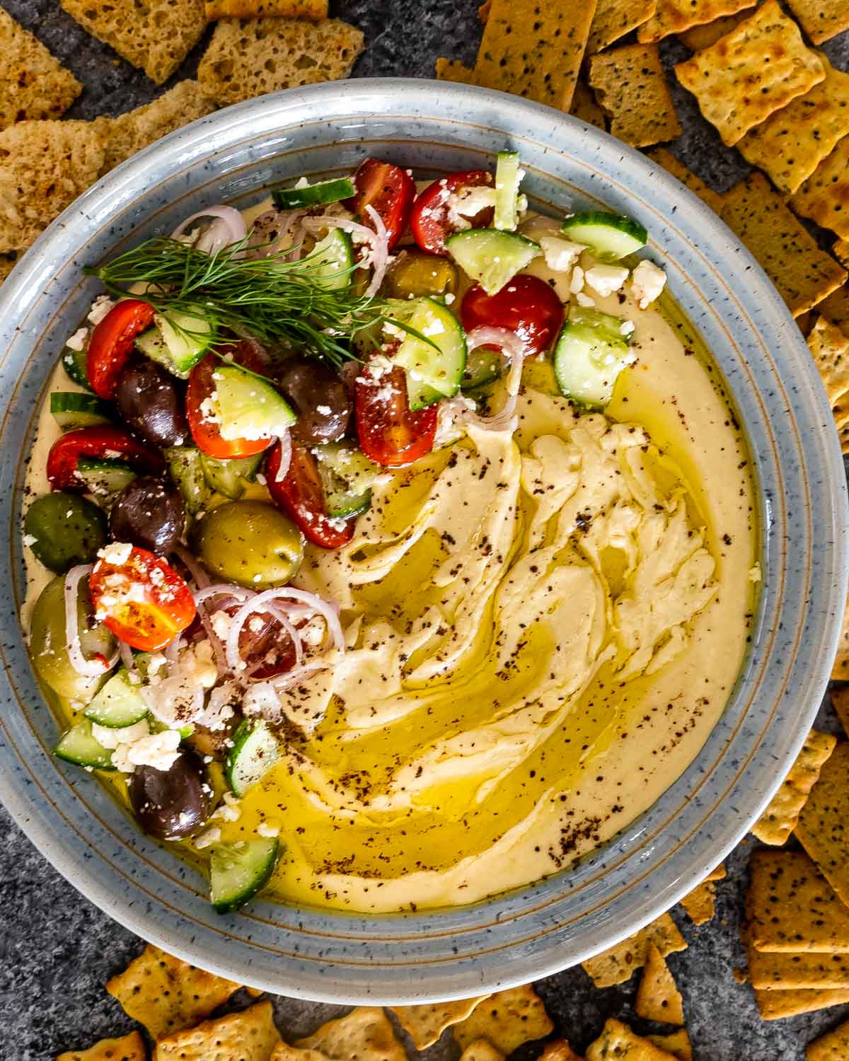 freshly made hummus drizzled with olive oil and garnished with tomatoes cucumbers and olives.