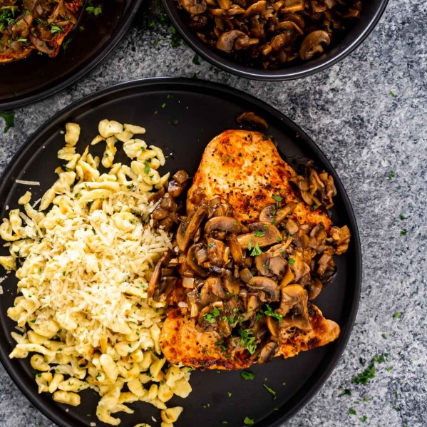 jagerschnitzel with spaetzle on a black plate garnished with parsley.