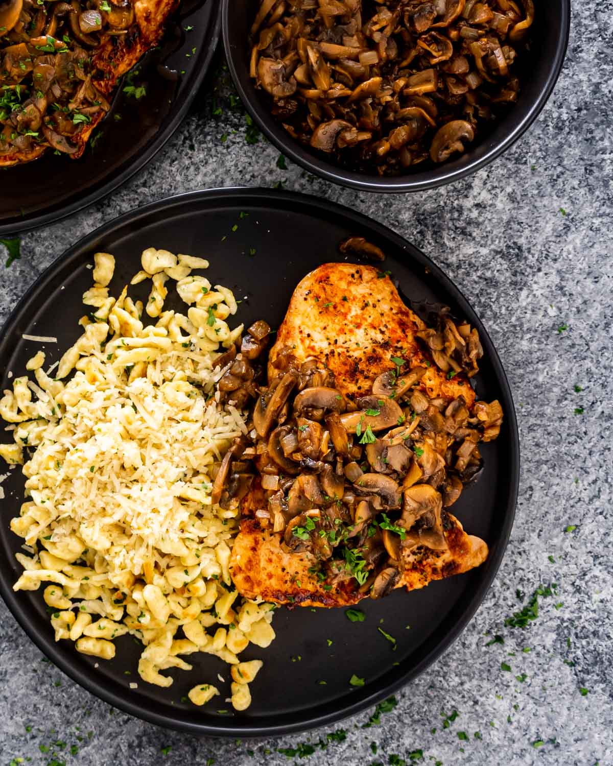 jagerschnitzel with spaetzle on a black plate garnished with parsley.