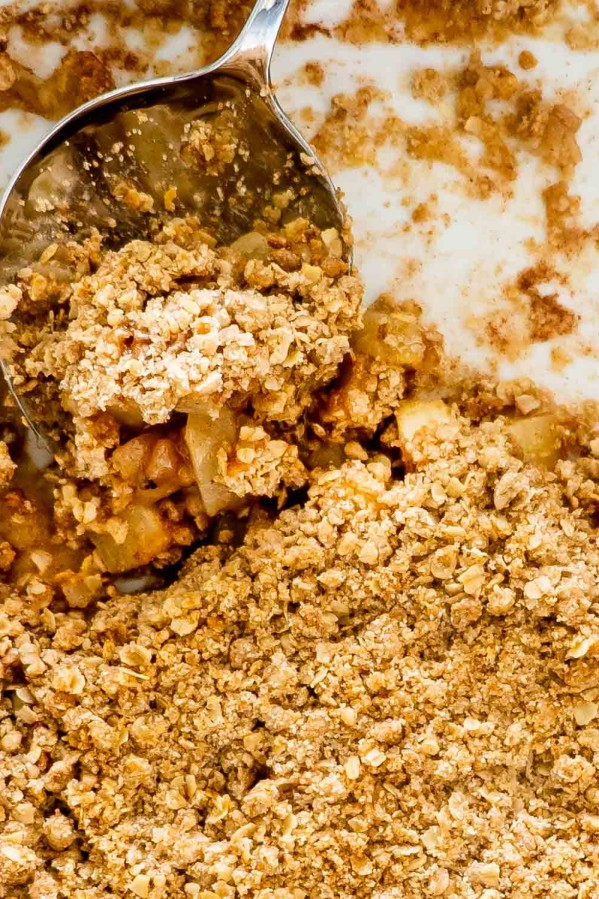 apple crumble in a baking dish with a serving spoon inside.