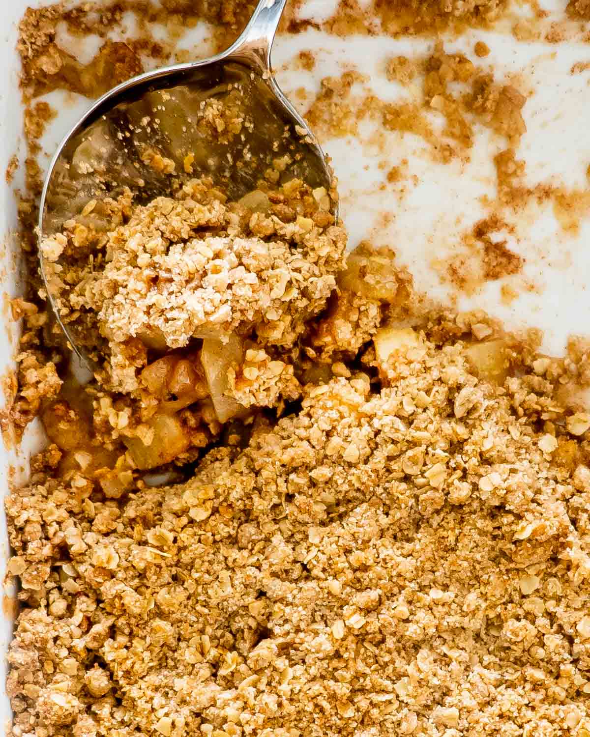 apple crumble in a baking dish with a serving spoon inside.