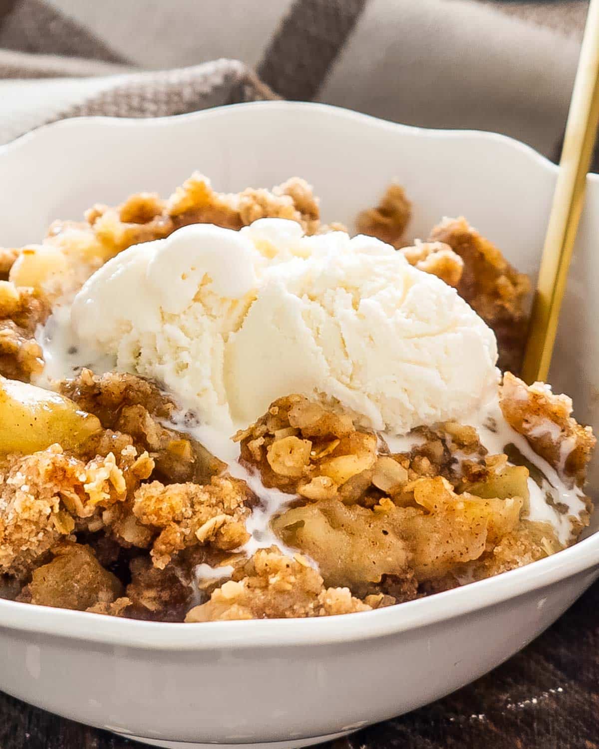a bowl filled with apple crumble and a scoop of ice cream and a spoon inside.