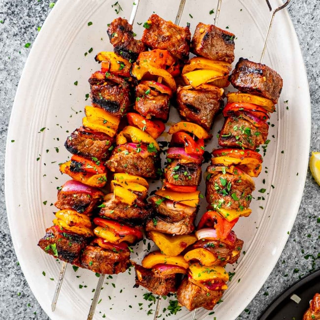beef shish kebab skewers on a white serving platter.