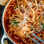 bucatini all'amatriciana in a pot with tongs twisting some pasta.