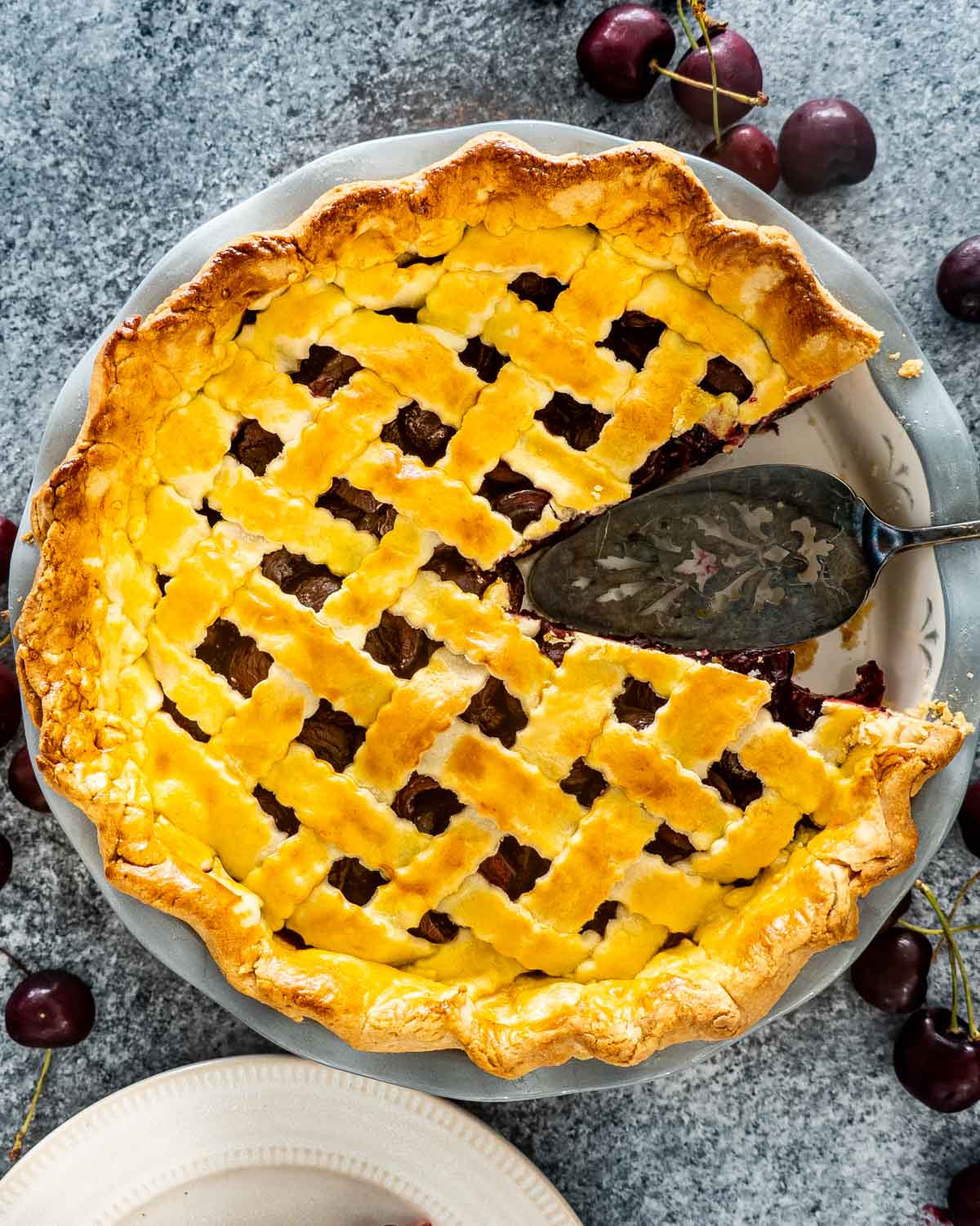 overhead shot of cherry pie with a slice missing and a serving spatula in it.