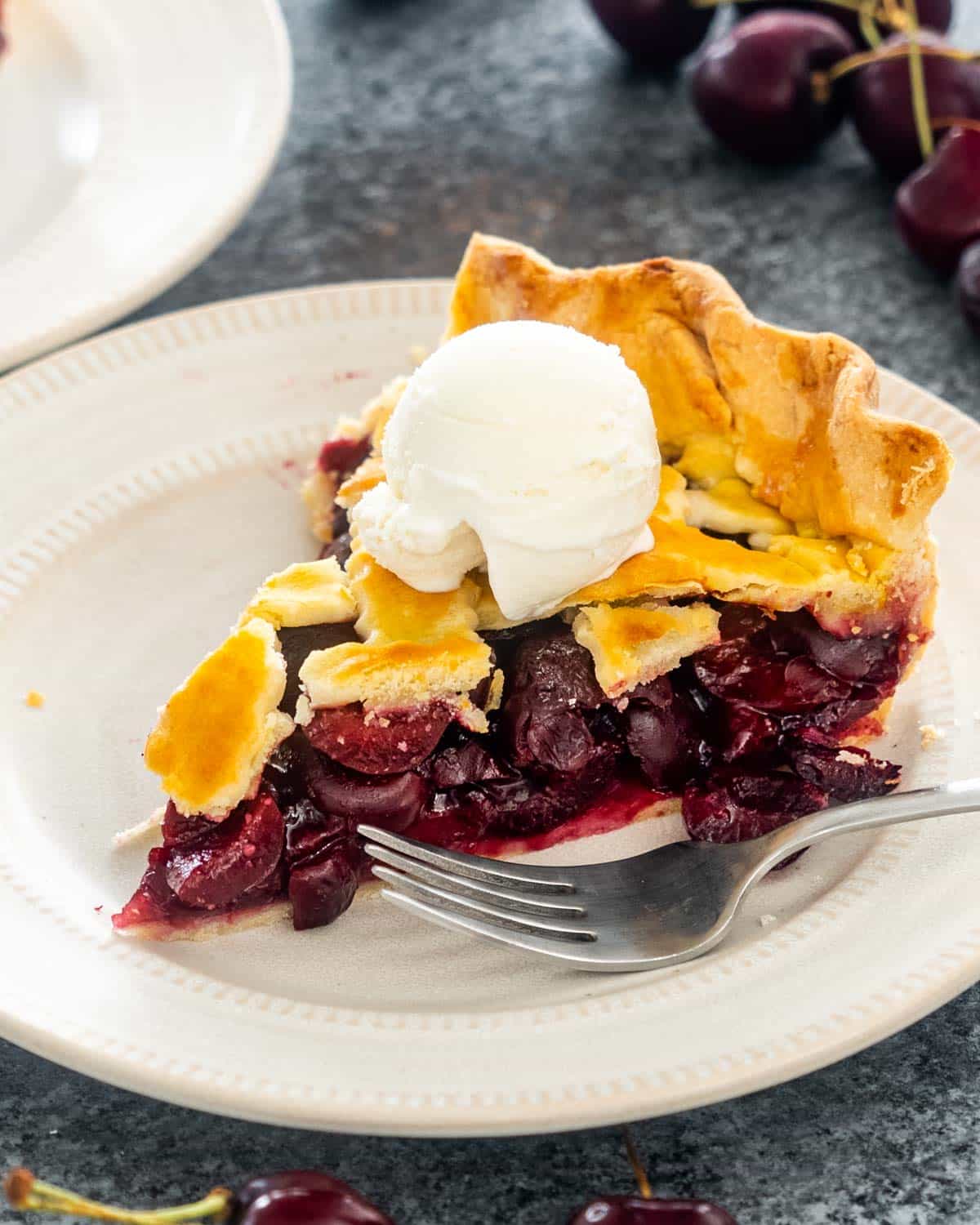 a slice of cherry pie on a plate with a scoop of ice cream.