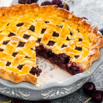 a cherry pie in a pie plate with a slice missing.