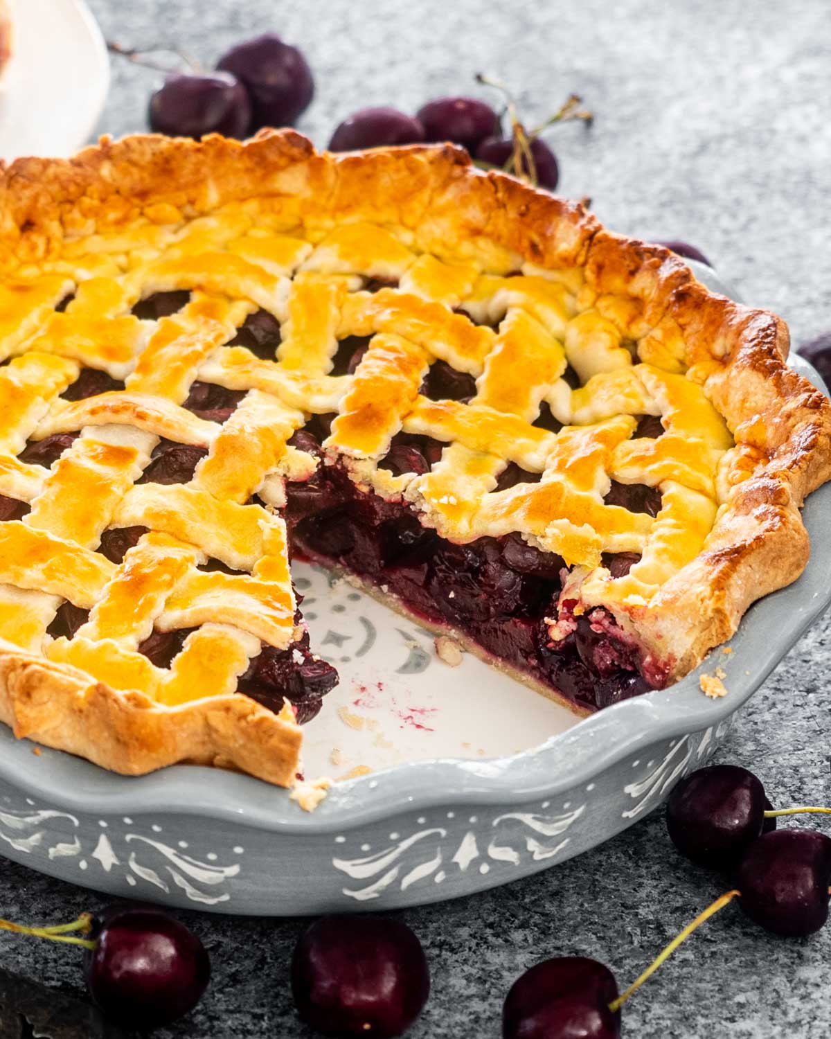 a cherry pie in a pie plate with a slice missing.