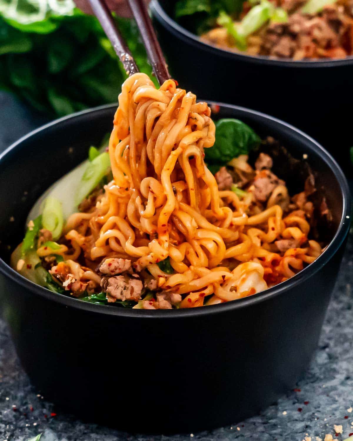 a pair of chop sticks lifting up some dan dan noodles from a bowl.