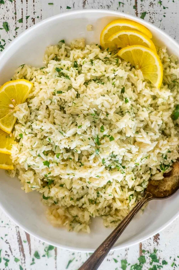 greek rice in a white bowl garnished with lemon slices.