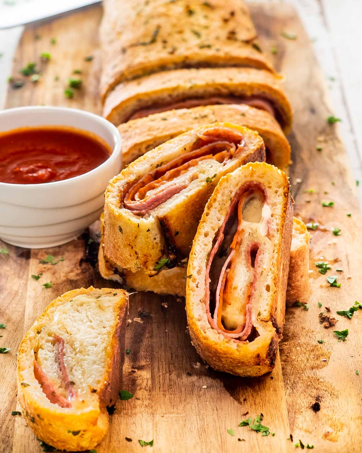 a freshly made stromboli cut into pieces on a cutting board next to a bowl with marinara.