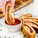 a hand dipping a piece of stromboli in a bowl with marinara sauce.